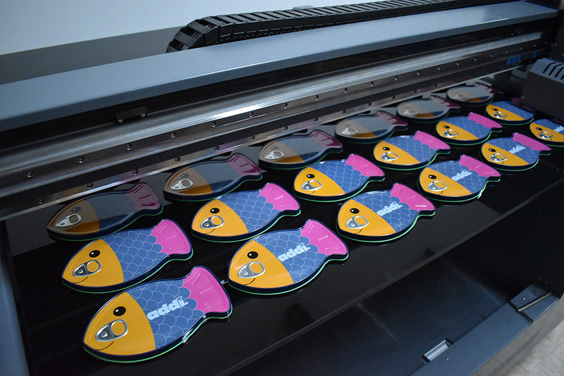 Digitaldruckmaschine bei ADV PAX Lutec, erste Reihe der Fish Tin Sonderform-Fischdosen bereits mit Kundenlogo personalisiert – hochwertige Metallverpackungen in Produktion.