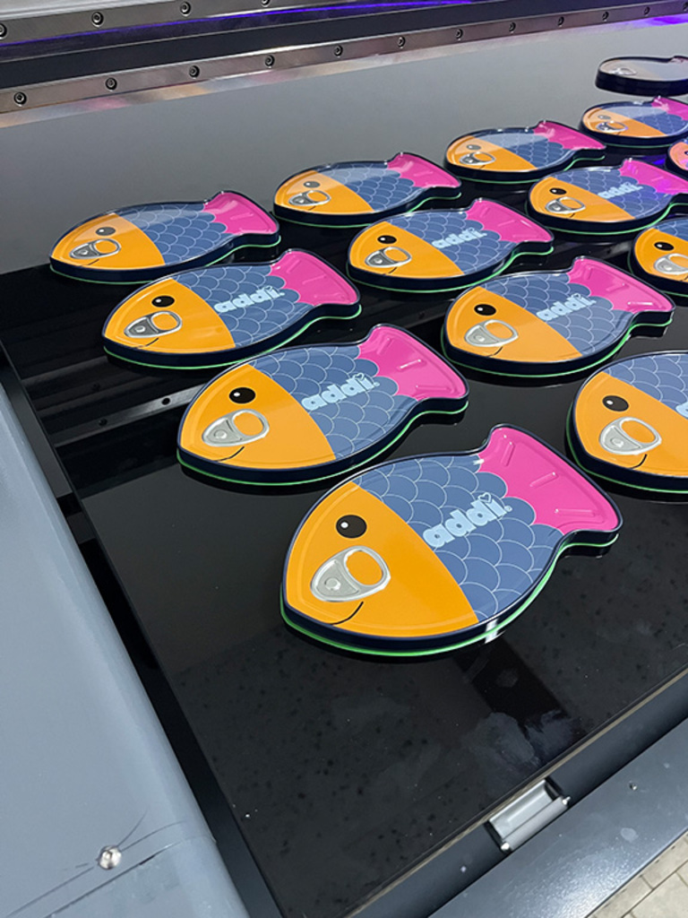 Fertig bedruckte Fish Tin Sonderform-Fischdosen auf der Digitaldruckmaschine bei ADV PAX Lutec – individuell personalisierte Weißblechdosen mit Kundenlogo.
